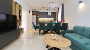 Un salon moderne doté d’un téléviseur à écran plat, d’un coin repas avec des chaises, d’un canapé et d’une cuisine en arrière-plan.