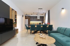 Ein modernes Wohnzimmer mit Flachbildfernseher, einer Essecke mit Stühlen, einer Couch und einer Küche im Hintergrund.