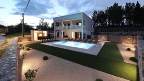 Une maison moderne à deux étages, dotée d’une piscine, d’un espace salon extérieur et d’un mur en pierre.