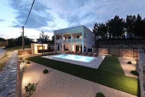 Ein modernes, zweistöckiges Haus mit Schwimmbad, Sitzgelegenheit im Freien und einer Steinmauer.