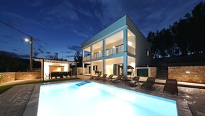 Une maison moderne à deux étages, dotée d’une piscine, d’un espace salon extérieur et d’un mur en pierre.