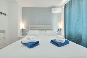 Ein Hotelzimmer mit einem Bett, zwei Nachttischen, einer Wand-Klimaanlage und einem Vorhangfenster.