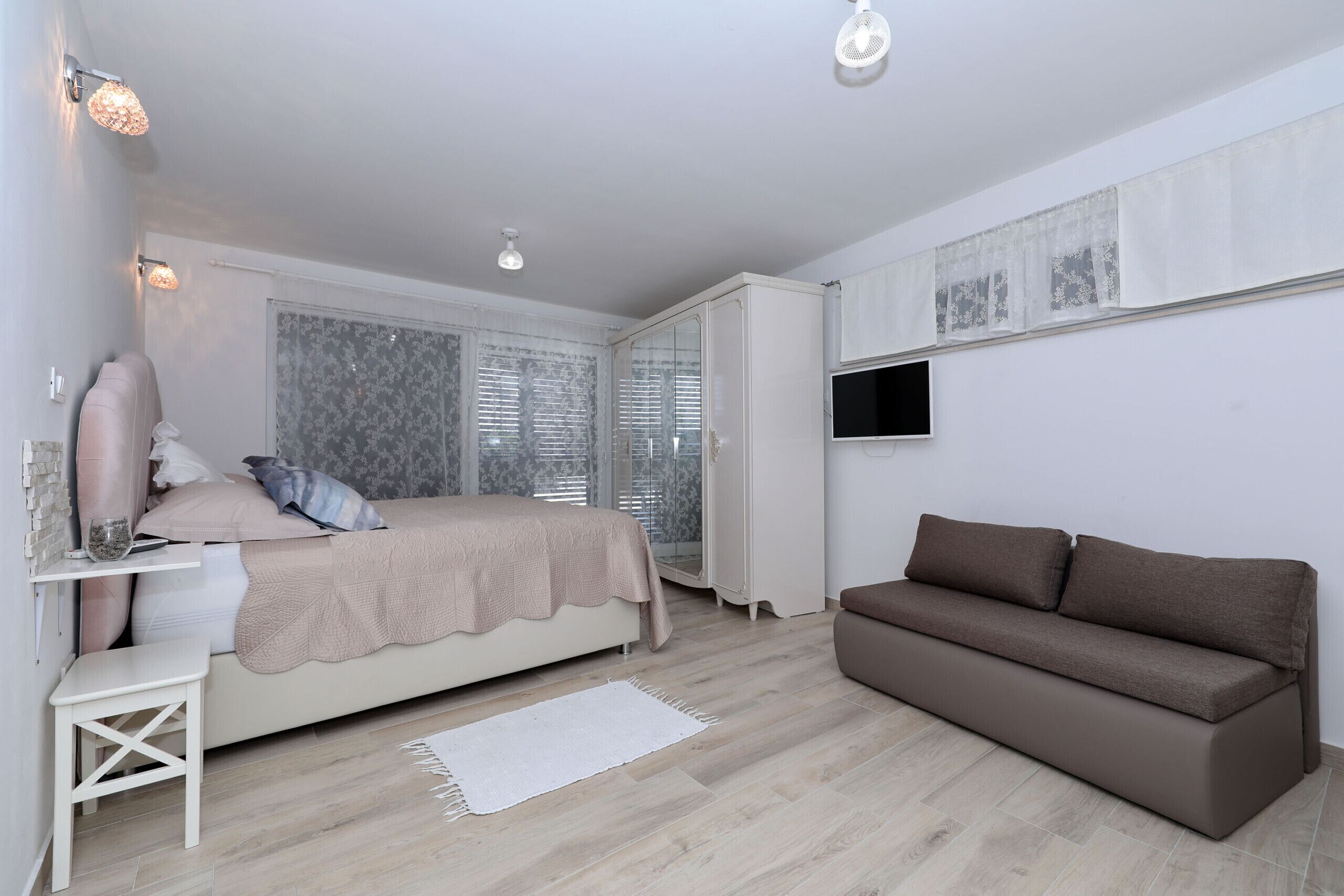 A bedroom with a bed, a sofa, a TV, and a window with blinds.