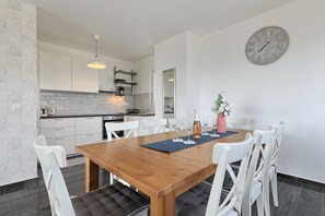 Eine moderne Küche mit weißen Schränken, einem Holztisch und einer Wanduhr.