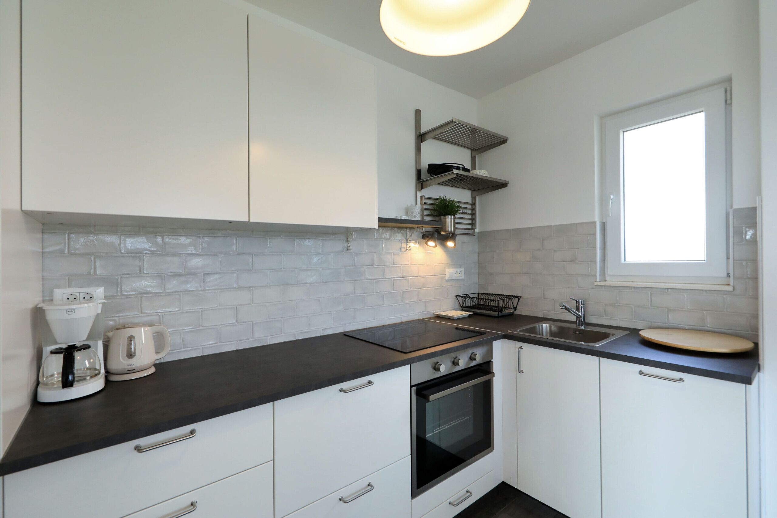 A modern kitchen with white cabinets, a black countertop, a built-in oven, a sink, and a window.