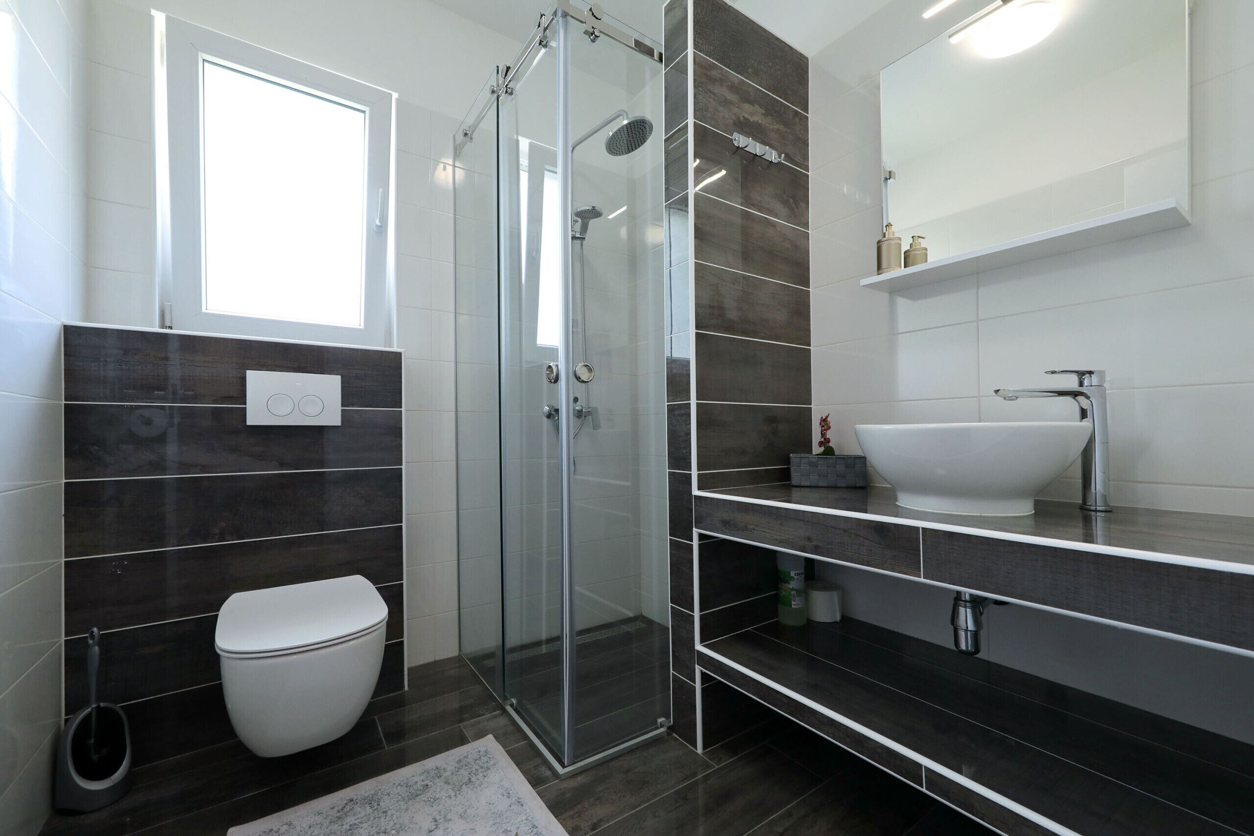 A modern bathroom with a glass-enclosed shower, a white toilet, a large white sink, and a mirror above the sink.