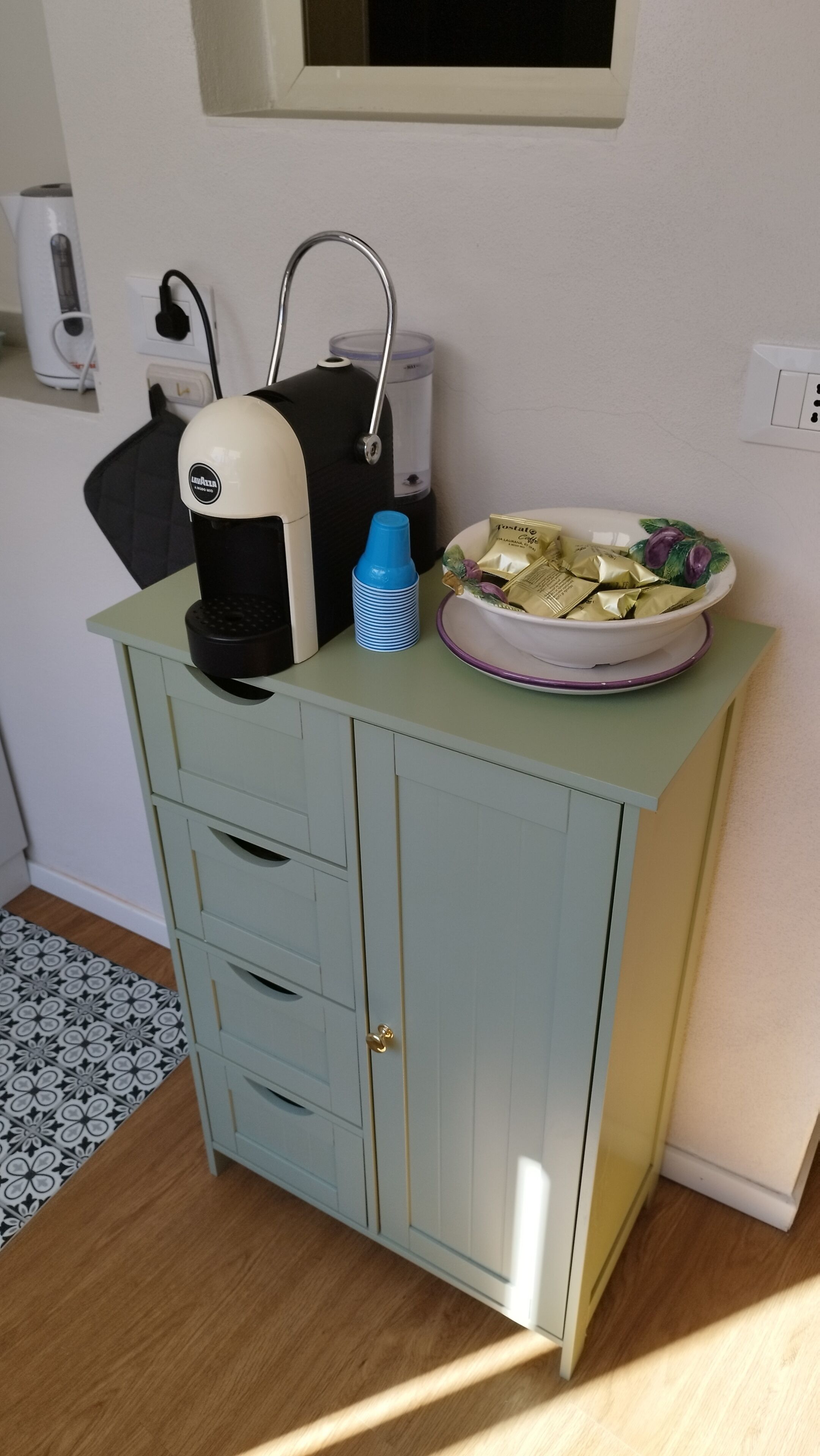Une petite cuisine équipée d’une machine à café, d’un distributeur d’eau et d’un bol de nourriture posé sur le comptoir.