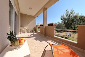Ein Balkon mit Tisch, auf dem Obst, Stühle und ein Blick auf den Garten liegen.