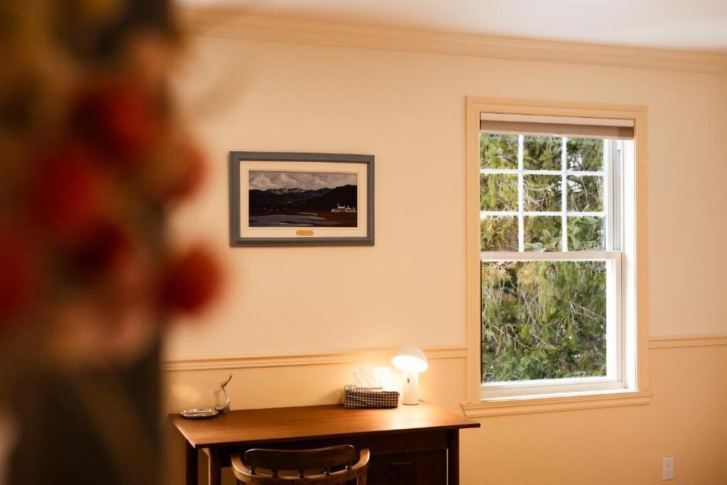 Una habitación con un escritorio, un cuadro en la pared y una ventana con vistas a zonas verdes.