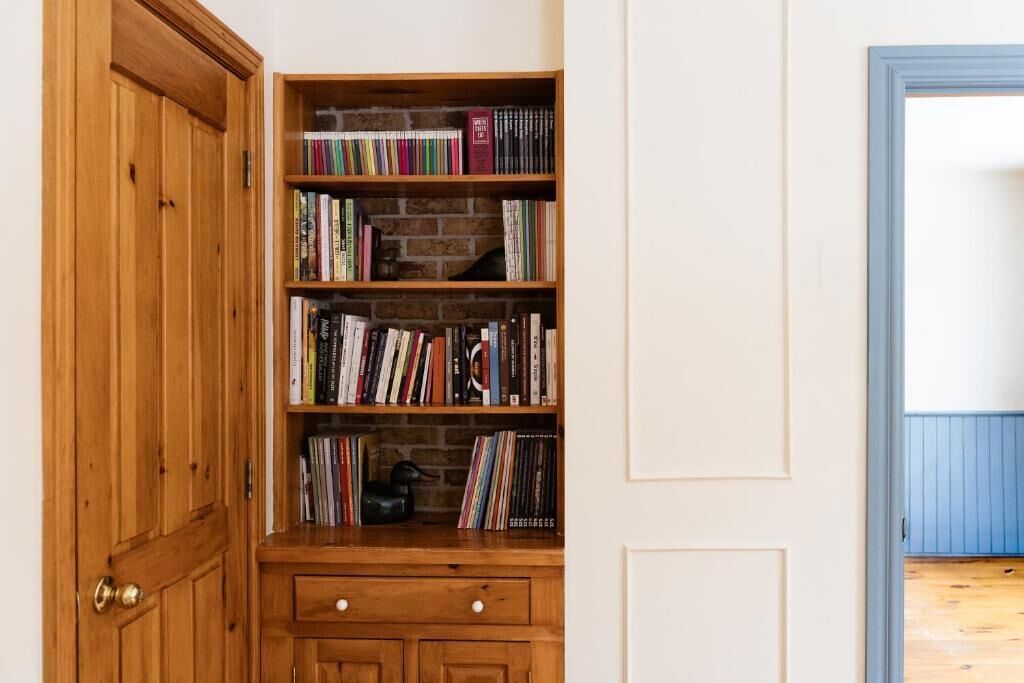 Una estantería de madera con libros, un cajón pequeño y un fondo de pared de ladrillo.