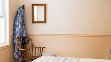 A bedroom with a bed, a wooden chair, a window, and a wall-mounted mirror.