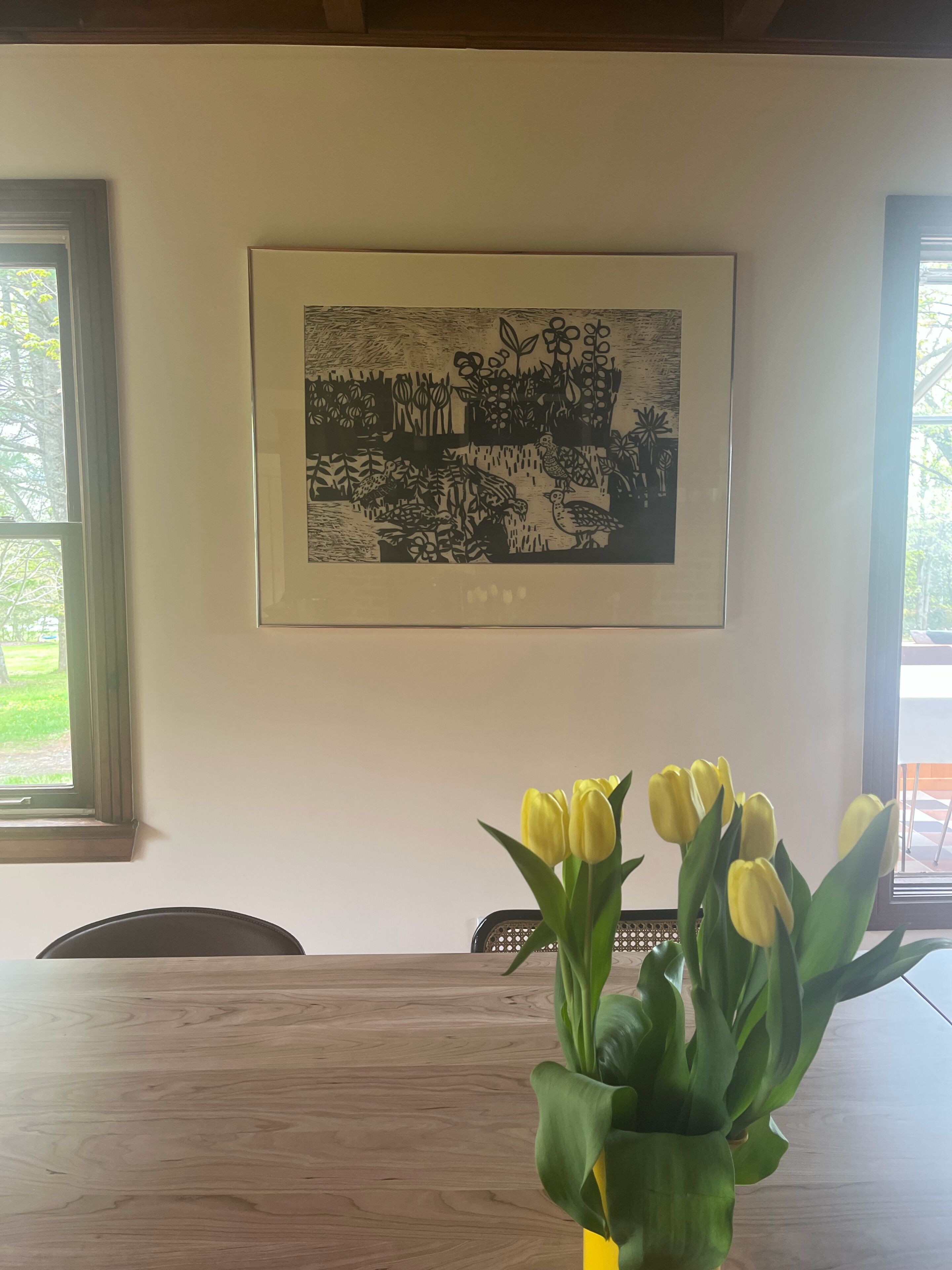 A dining area with a table, chairs, a framed artwork, and a vase of yellow tulips.