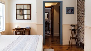 Un dormitorio con cama, escritorio, silla, espejo y puerta que da a un pasillo.