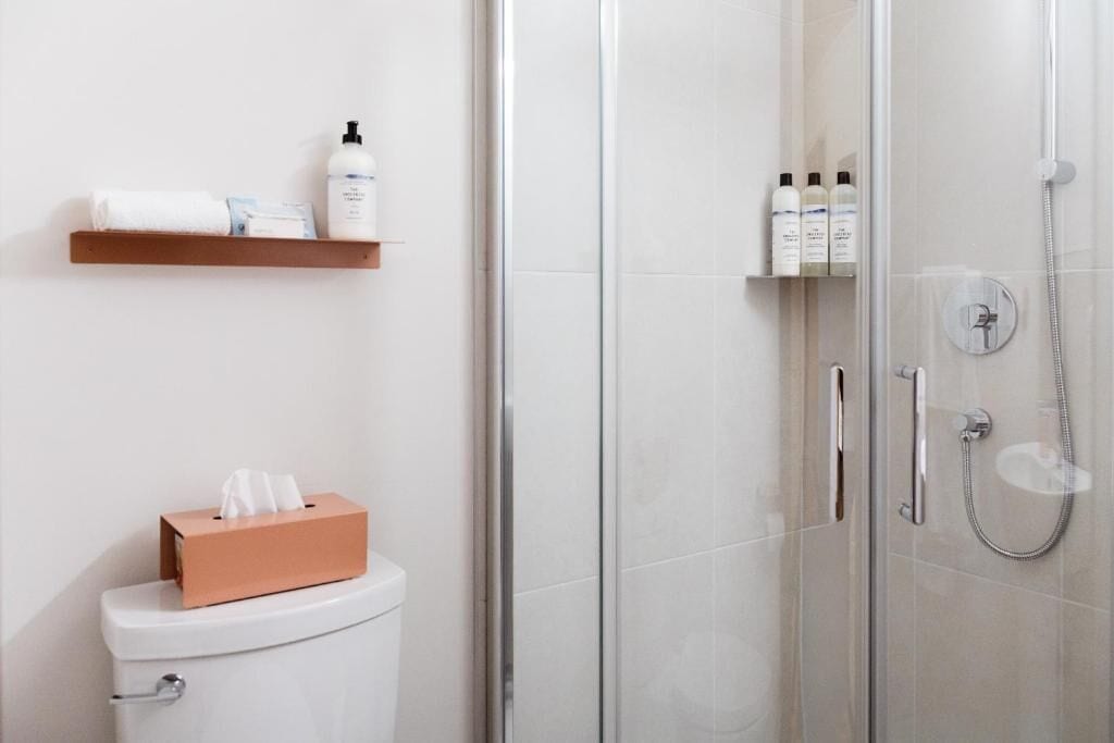 Un baño moderno con inodoro, cabina de ducha de vidrio y repisas con artículos de aseo.