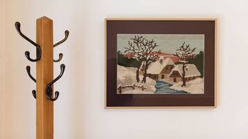 A framed cross-stitch artwork on a wall, a wooden coat rack with hooks, and a plain wall.
