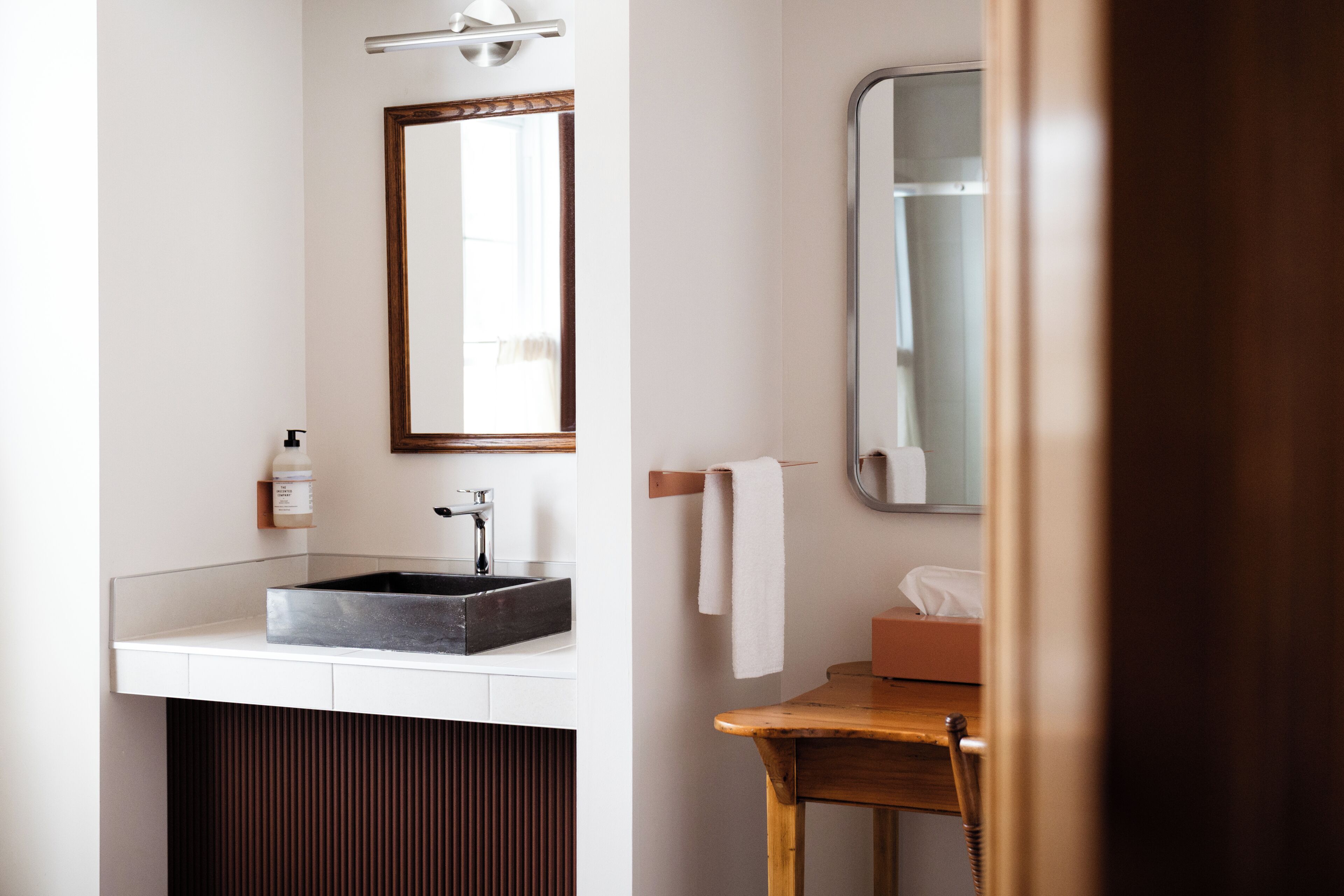 Une salle de bain équipée d’un lavabo, d’un miroir, d’un porte-serviettes et d’une chaise en bois.