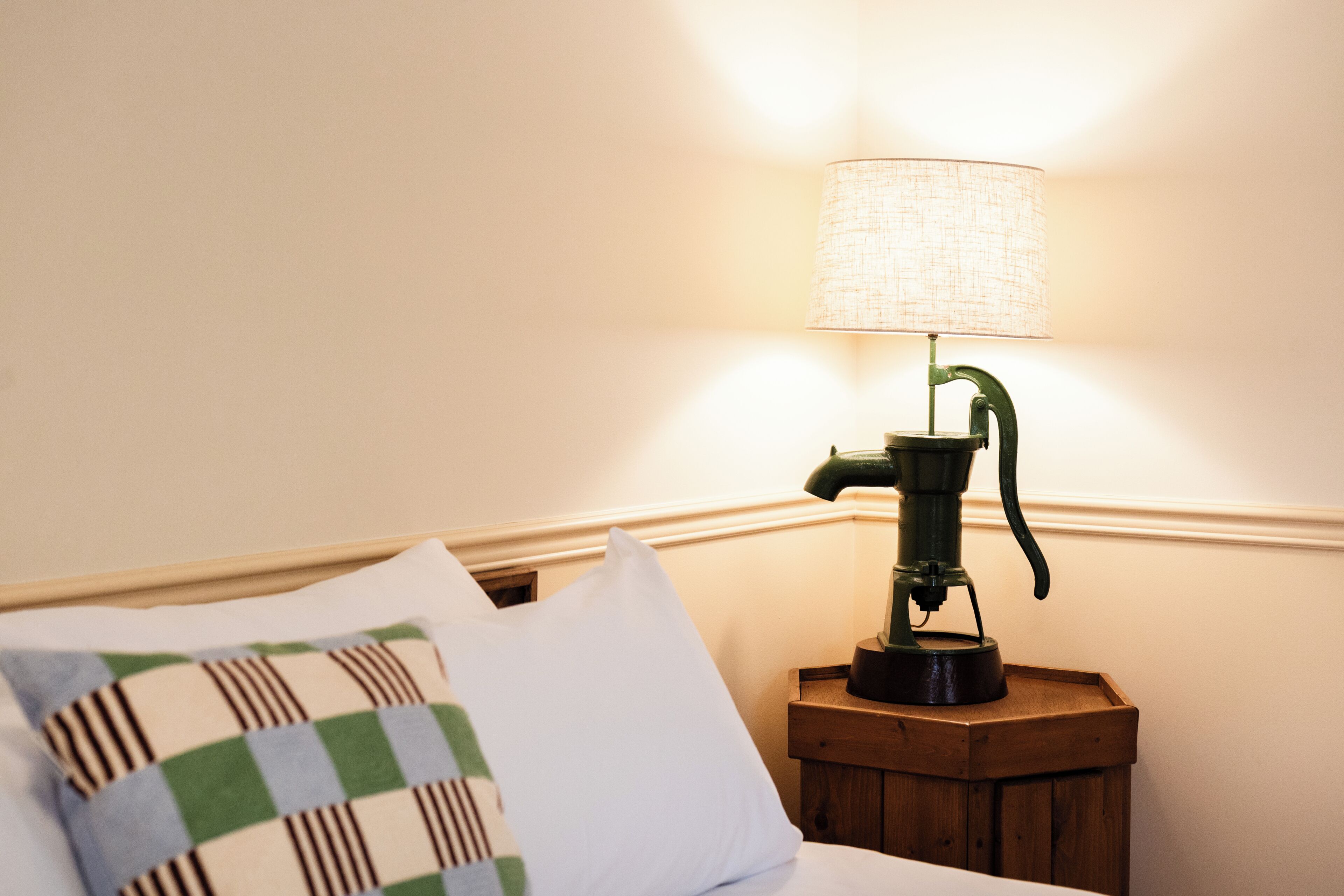 Ein Bett mit einem karierten Kopfkissen, ein Nachttisch mit einer Lampe und ein Holznachttisch.