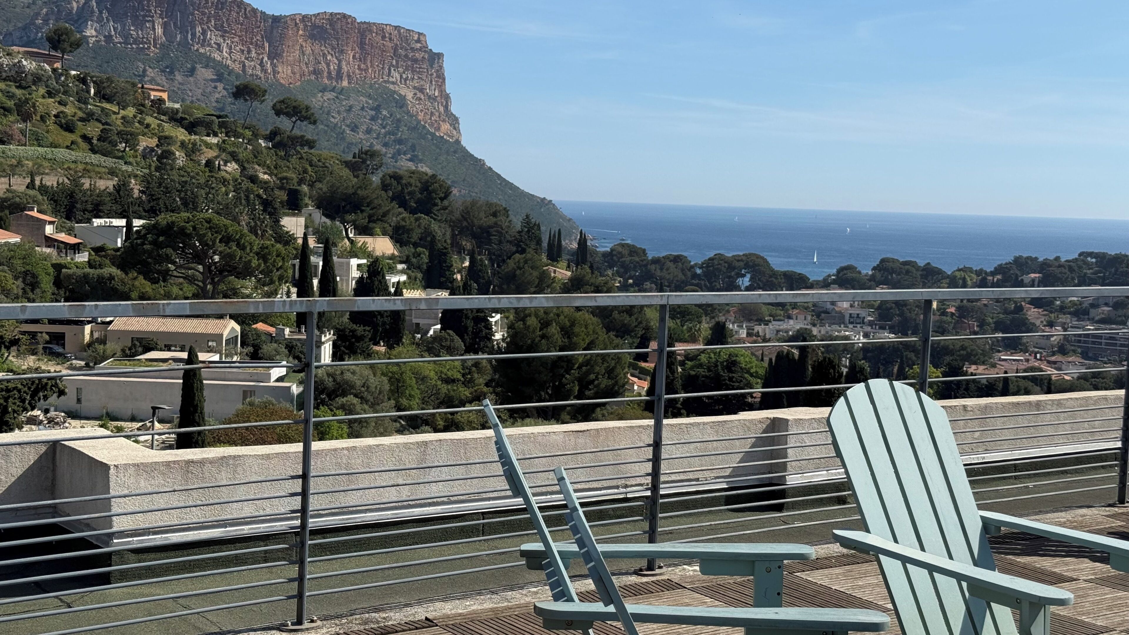 A balcony with a view of a coastal town, a chair, and a railing.