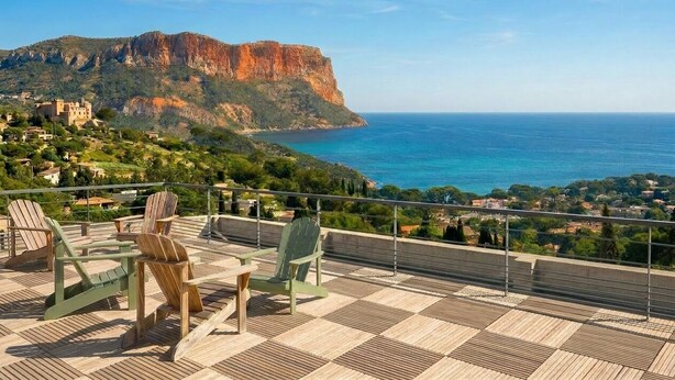 Eine Terrasse mit Stühlen und Blick auf eine Küstenlandschaft mit einer markanten Klippe.