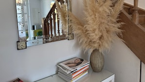 Ein Spiegel mit floralem Dekor, eine Vase mit Pampasgras und ein Magazin-Stapel auf einer weißen Oberfläche.