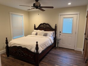 Un dormitorio con cama de madera, ventilador de techo y puerta con ventanal.