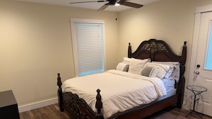 Quarto com cama de madeira, ventoinha no teto, janela com persianas e uma porta.