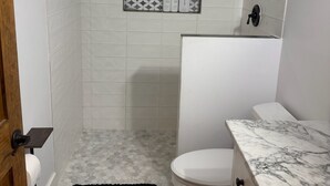 Casa de banho com sanita, chuveiro, bancada de mármore e painel de azulejos estampados.