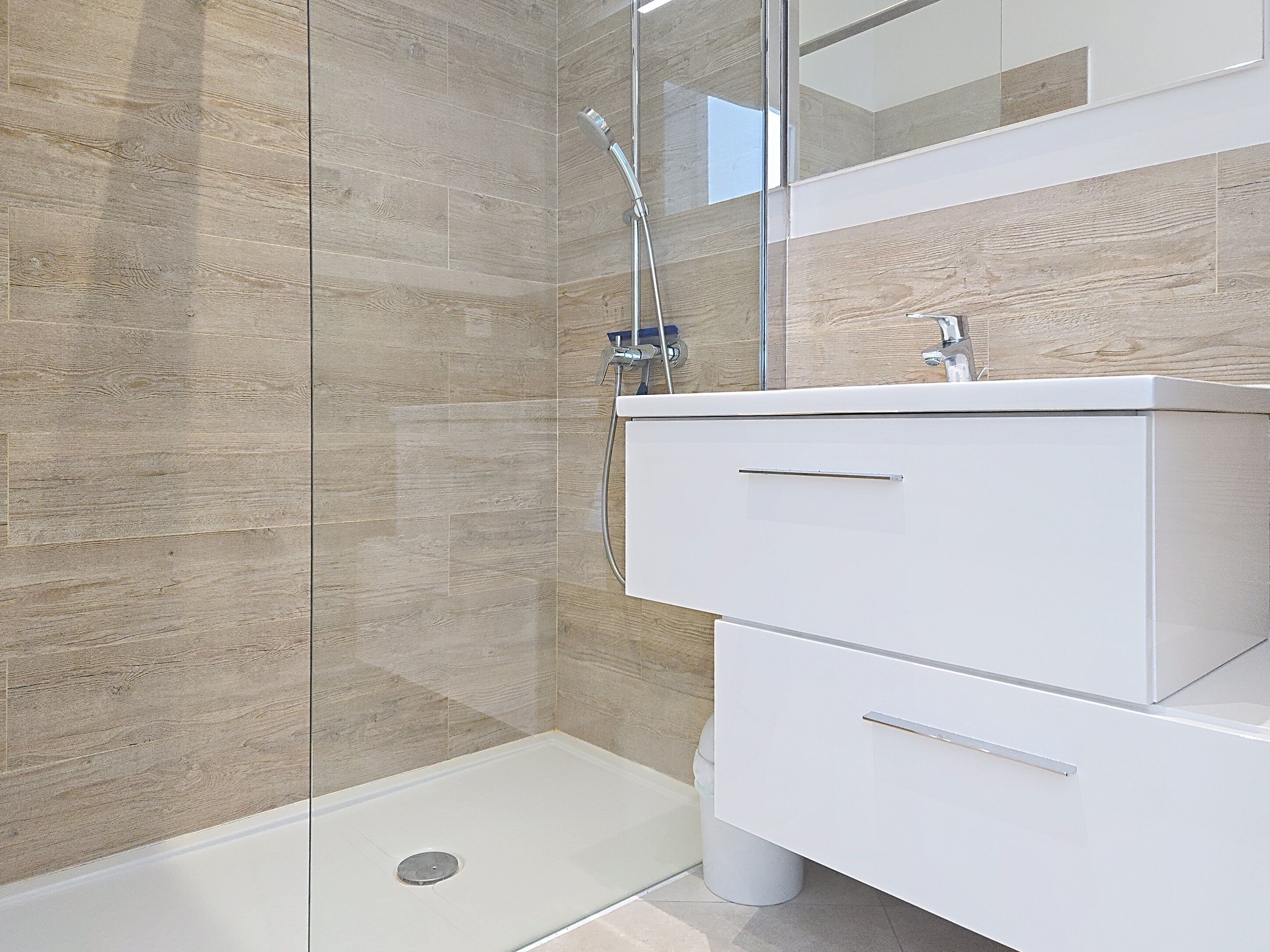 A modern bathroom with a glass shower enclosure, a white vanity with drawers, and a wooden wall panel.