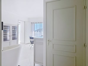 Ein heller Innenraum mit geschlossener Tür, einem Fenster mit Vorhängen und einem Sessel.