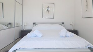Een hotelkamer met een bed, twee nachtkastjes, een grote spiegel en twee ingelijste kunstwerken aan de wand.