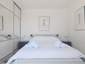 Ein Hotelzimmer mit einem Bett, zwei Nachttischen, einem großen Spiegel und zwei gerahmten Bildern an der Wand.