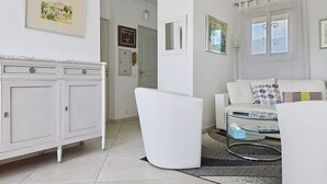 Een woonkamer met een witte bank, een glazen salontafel, een witte kast en een deur naar een andere kamer.