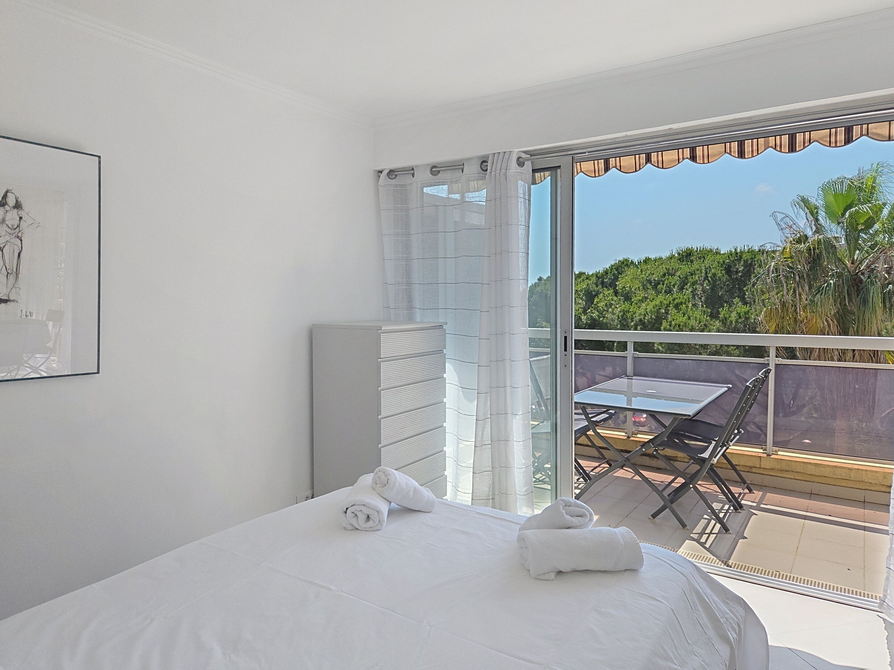 Habitación de hotel con cama, una mesa y sillas en un balcón con vistas a la vegetación.