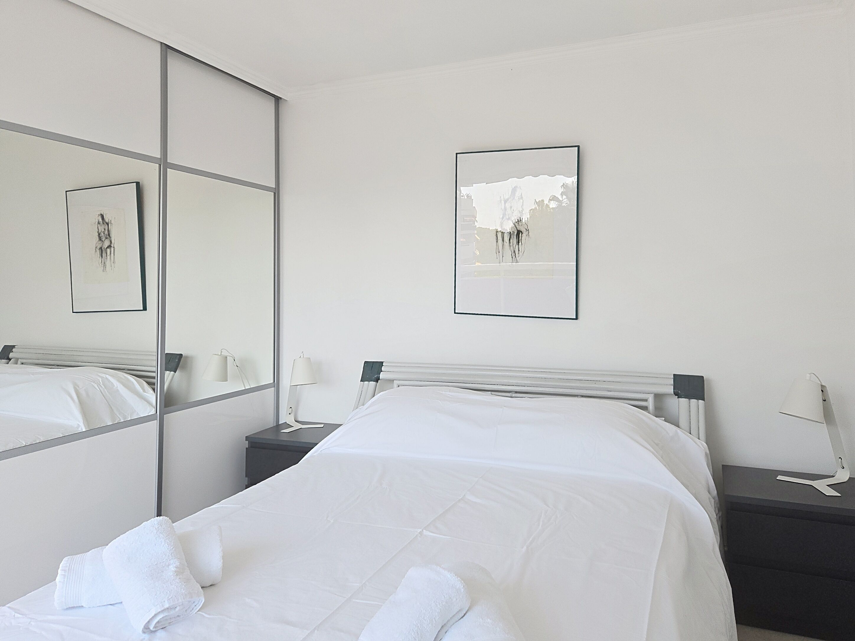 Une chambre d’hôtel avec un lit, une table de chevet, une lampe, un miroir et deux tableaux encadrés accrochés au mur.