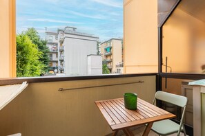 Ein Balkon mit Tisch und Stuhl, einem grünen Eimer und Blick auf Gebäude.