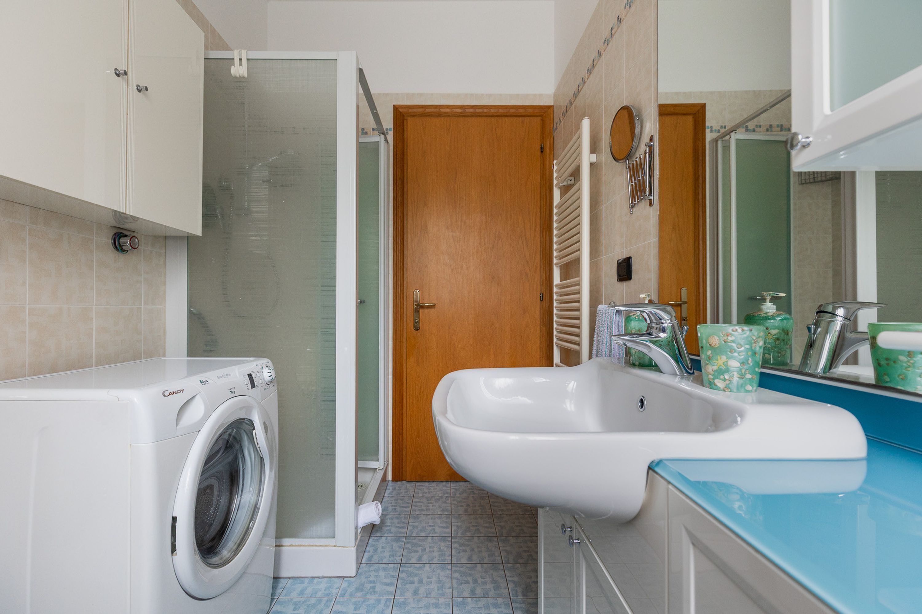 Ein kleines Badezimmer mit Waschmaschine, Waschbecken und Dusche.