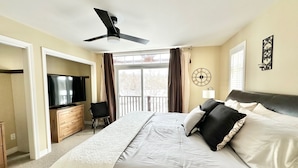 A hotel room with a bed, a television, a desk, and a balcony with curtains.