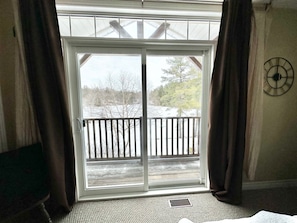 A room with a large sliding glass door leading to a balcony with a wooden railing.