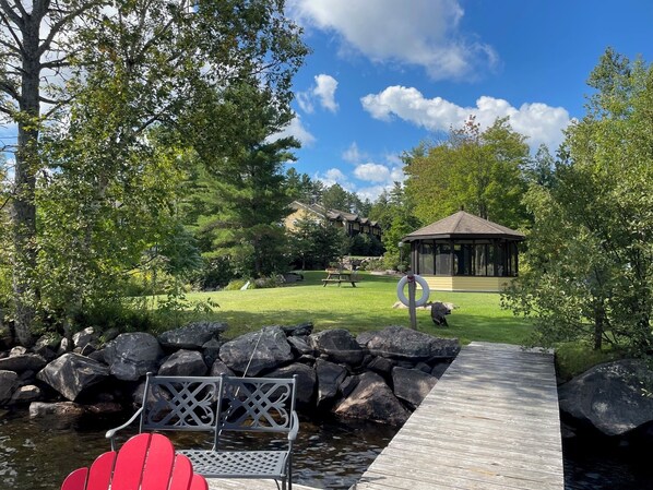 Eine Holzstege, der zu einem Teich mit Steinen, einem Pavillon und einer Picknickgegend in einer Parkanlage führt.