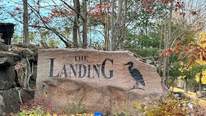 A stone sign with 'THE LANDING' and a bird engraving, surrounded by autumn foliage and rocks.