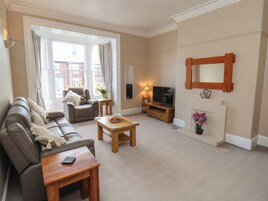 Una sala de estar con sofá, sillón, mesa de centro, televisor, chimenea y ventanas amplias.