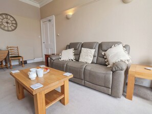 A living room with a sofa, a wooden coffee table, a clock, and a door. - Time Out (Whitby)