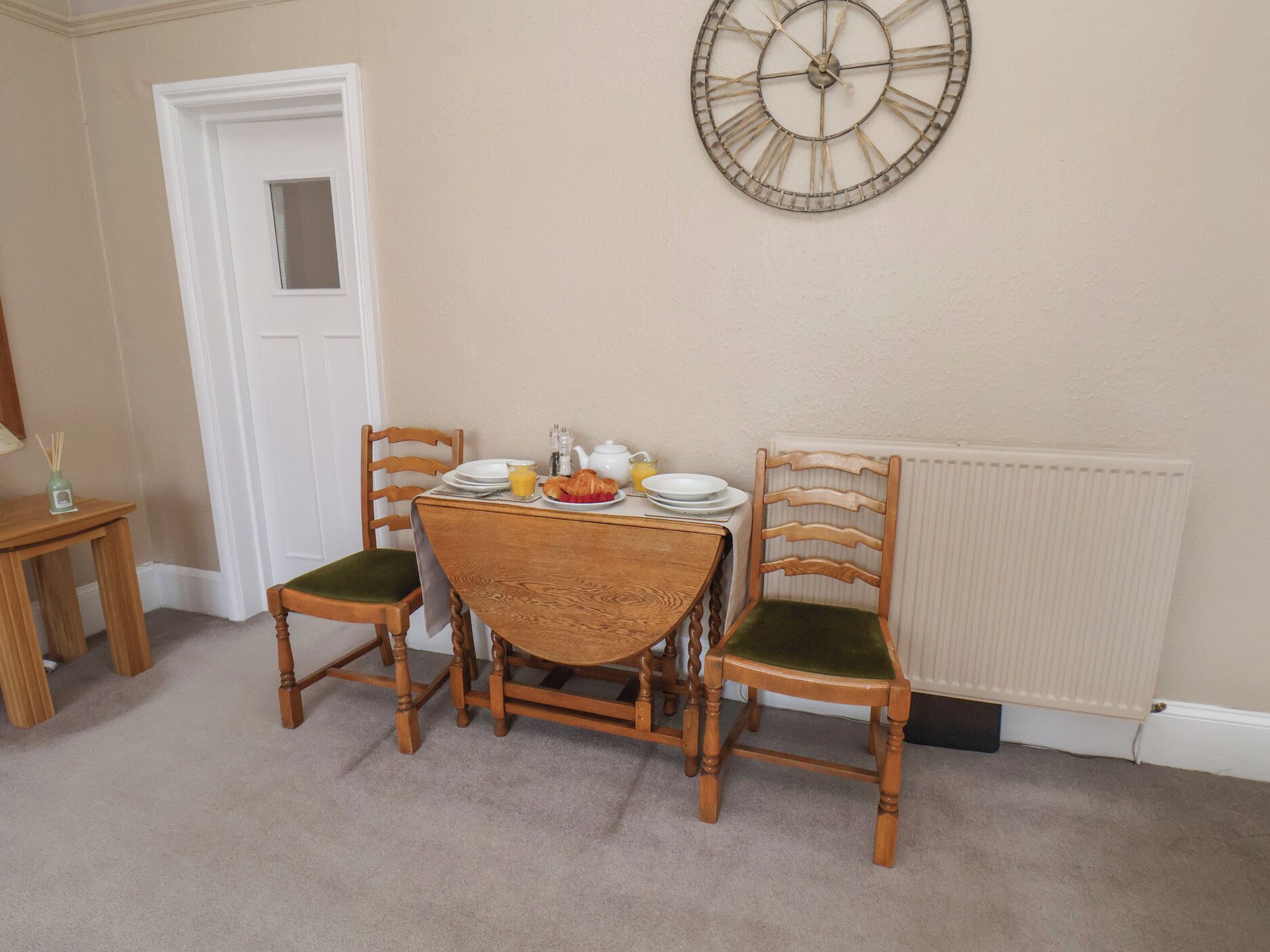 A dining area with a wooden table and chairs, a wall clock, and a radiator.