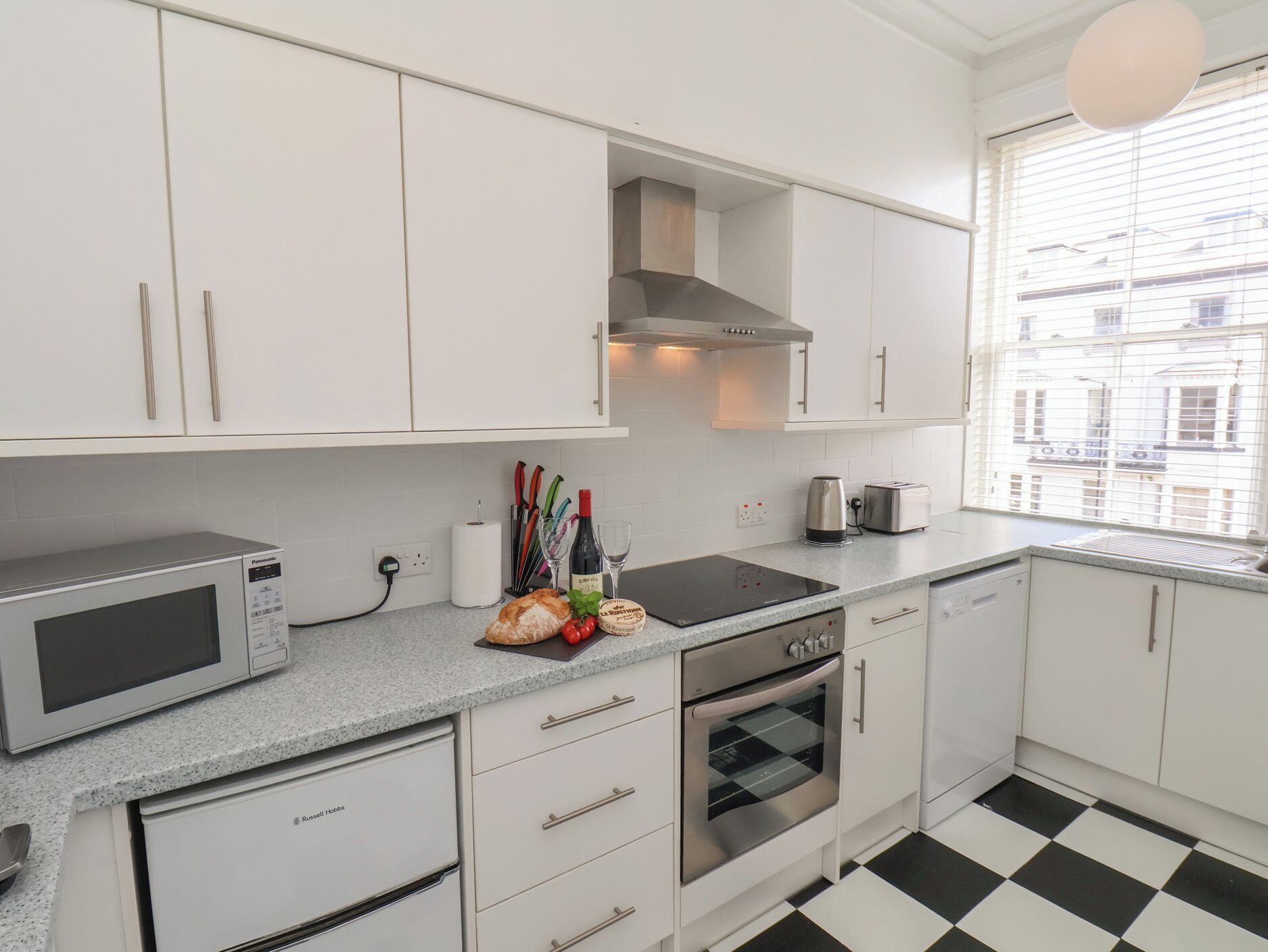 Una cocina moderna con armarios blancos, microondas, horno y ventana con vista a edificios.