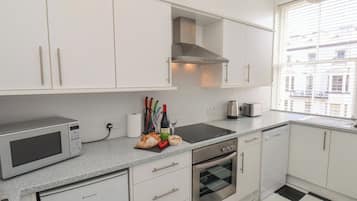 Una cocina moderna con armarios blancos, microondas, horno y ventana con vista a edificios.