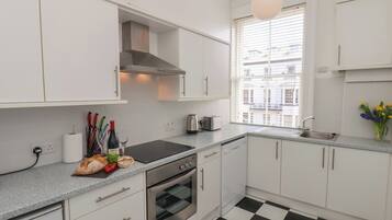 A modern kitchen with white cabinets, a black and white checkered floor, a stainless steel oven, and a window with blinds.