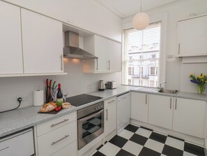 A modern kitchen with white cabinets, a black and white checkered floor, a stainless steel oven, and a window with blinds. - Time Out (Whitby)