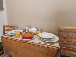 A breakfast table with croissants, raspberries, a teapot, and a glass of orange juice.