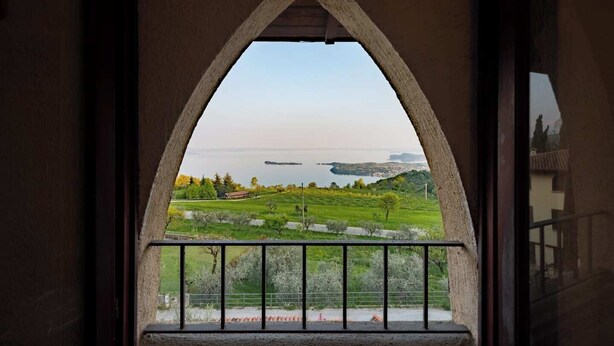 Vista attraverso una finestra ad arco in pietra su un paesaggio verde con alberi e un corpo d'acqua.