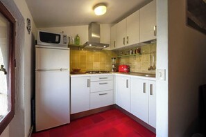 Eine kleine Küche mit weißen Schränken, einer Mikrowelle, einem roten Toaster und einem Gasherd.